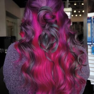 Person with long, wavy hair dyed in shades of magenta and purple, styled with a twisted section at the back.