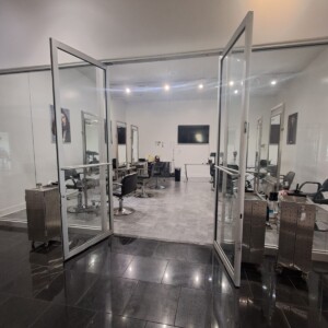 A modern hair salon with open glass doors, salon chairs, mirrors, and hairdressing equipment visible inside.