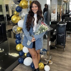 Screenshot Woman holding bouquet of flowers stands in front of balloon arrangement in a modern salon.