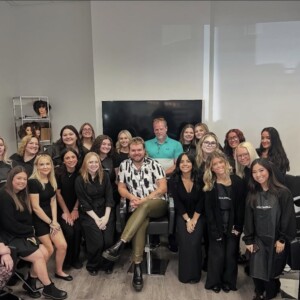 A group of people pose together in a salon, with some seated and others standing around them, all facing the camera.
