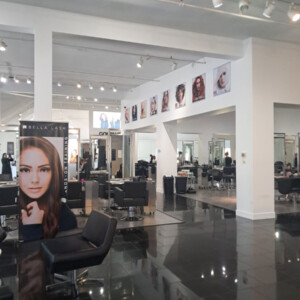 Modern hair salon interior with empty black chairs, large mirrors, and portraits of models displayed on the walls.