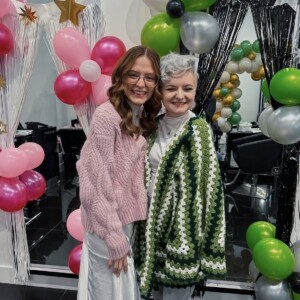 Screenshot Two people smiling and posing together at a party with balloon decorations and tinsel curtains in the background.