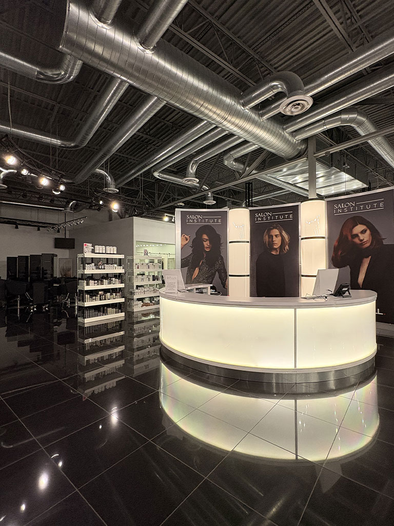 Modern salon reception area with illuminated desk, product shelves, and large model posters on the walls.